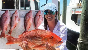 A smiling person is holding a large red snapper with other snappers hanging in the background, presumably after a successful fishing trip.