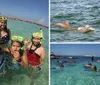 A group of six people wearing snorkeling gear takes a selfie while standing in shallow clear waters at a beach