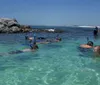 A group of people are snorkeling in clear shallow waters near a rock formation