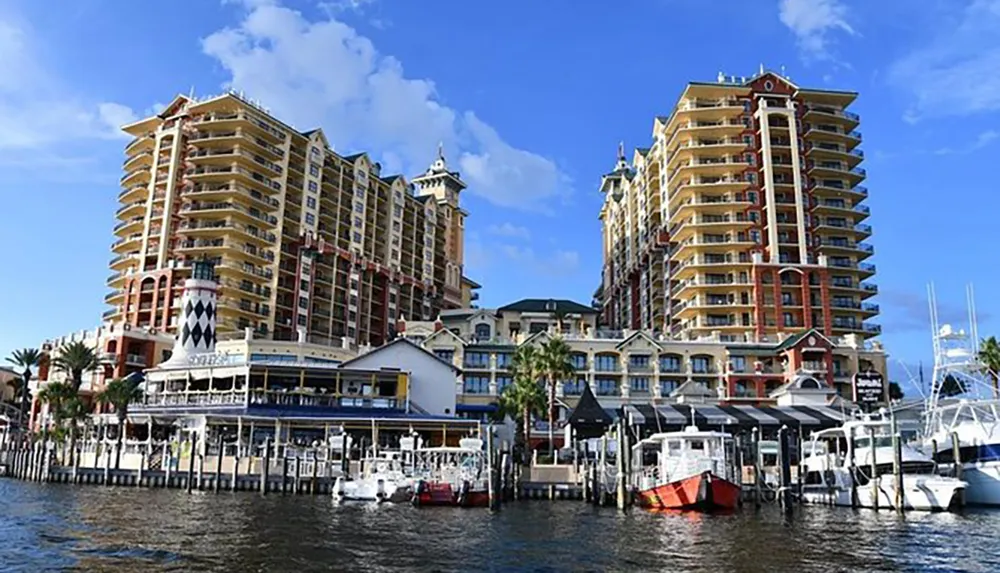 The image shows a waterfront scene with tall residential buildings along a dock with moored boats under a blue sky with scattered clouds