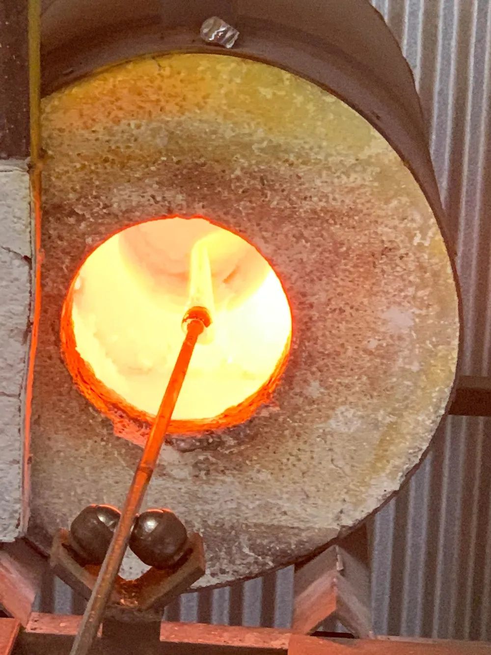 This image features a glowing glass furnace with an opening through which a glassblowers rod is inserted hinting at the process of glassblowing
