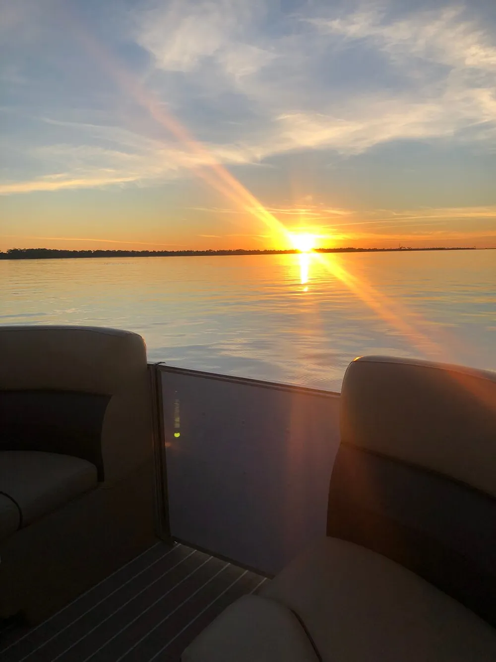The image captures a tranquil sunset with radiant beams of light stretching across the sky viewed from the deck of a boat on a calm body of water