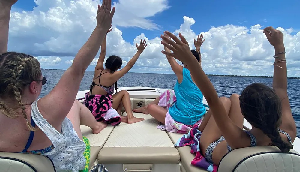 People are enjoying a boat ride on a sunny day with their hands raised in the air in what appears to be an expression of joy or excitement