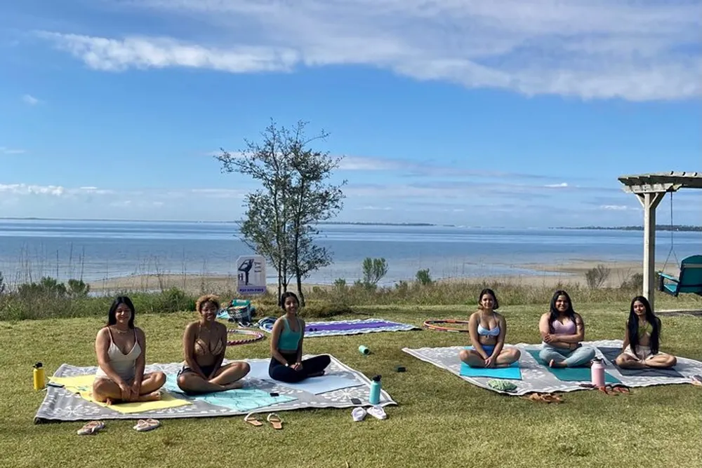 A group of people is enjoying an outdoor yoga session by a lakeside on a sunny day