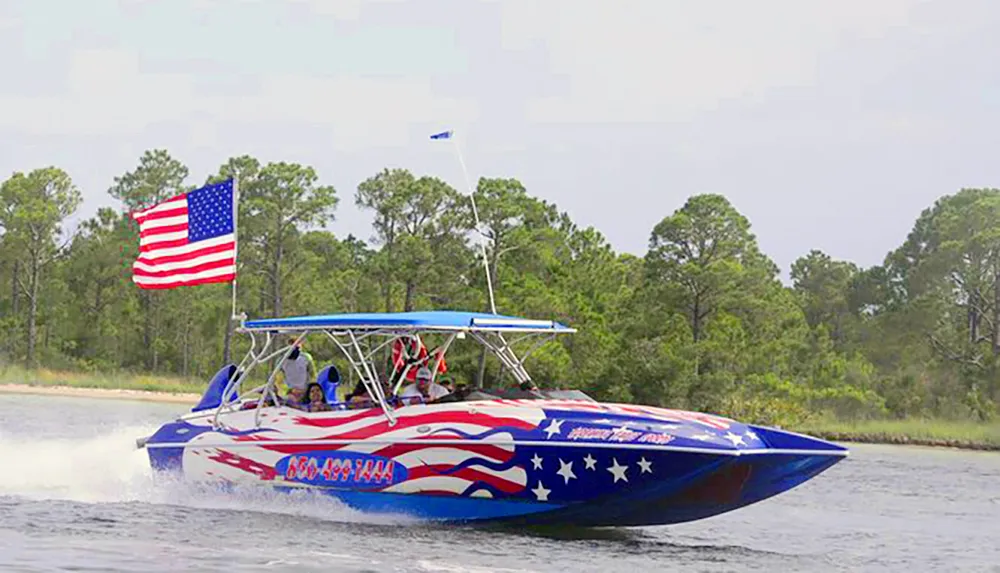 A speedboat adorned with an American flag design and an actual flag is cruising on the water with passengers on board