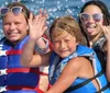 A group of people wearing life jackets are enjoying a ride on a yellow banana boat being pulled by a motorboat on a blue sea