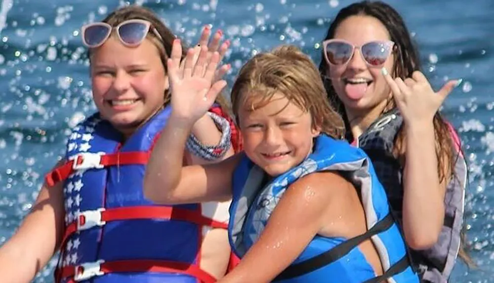 Three individuals are having a joyful time on the water waving and making playful gestures at the camera