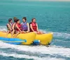 A group of people wearing life jackets are enjoying a ride on a yellow banana boat being pulled by a motorboat on a blue sea