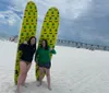 Three people each with different expressions stand on a sunny beach with two surfboards exuding a carefree vacation vibe
