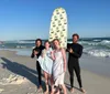 Three people each with different expressions stand on a sunny beach with two surfboards exuding a carefree vacation vibe