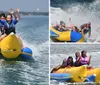 Three children are joyfully riding a banana boat on the water with their arms raised in excitement