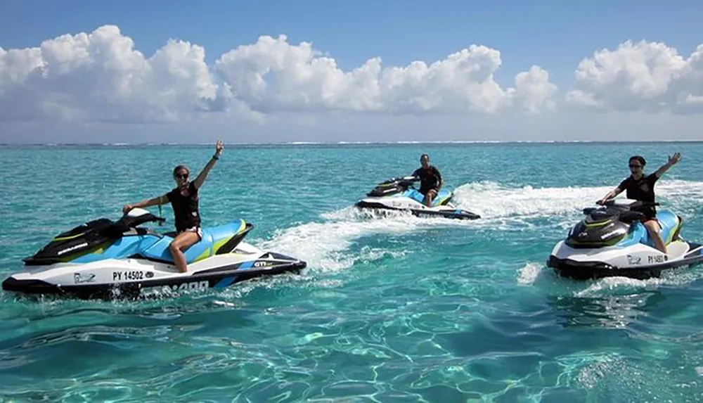 Three people are joyfully riding jet skis on a clear blue ocean