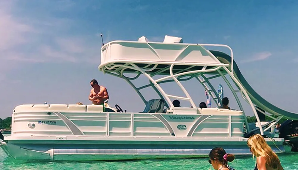 A person is preparing to dive from the upper deck of a pontoon boat into the turquoise water as others look on