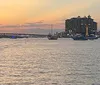 A group of six people is smiling and posing for a photo on a boat with a beautiful sunset over the water in the background