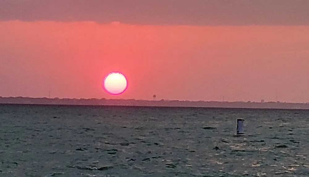 The image captures a vibrant pink and orange sunset over the ocean with a partially visible buoy in the water