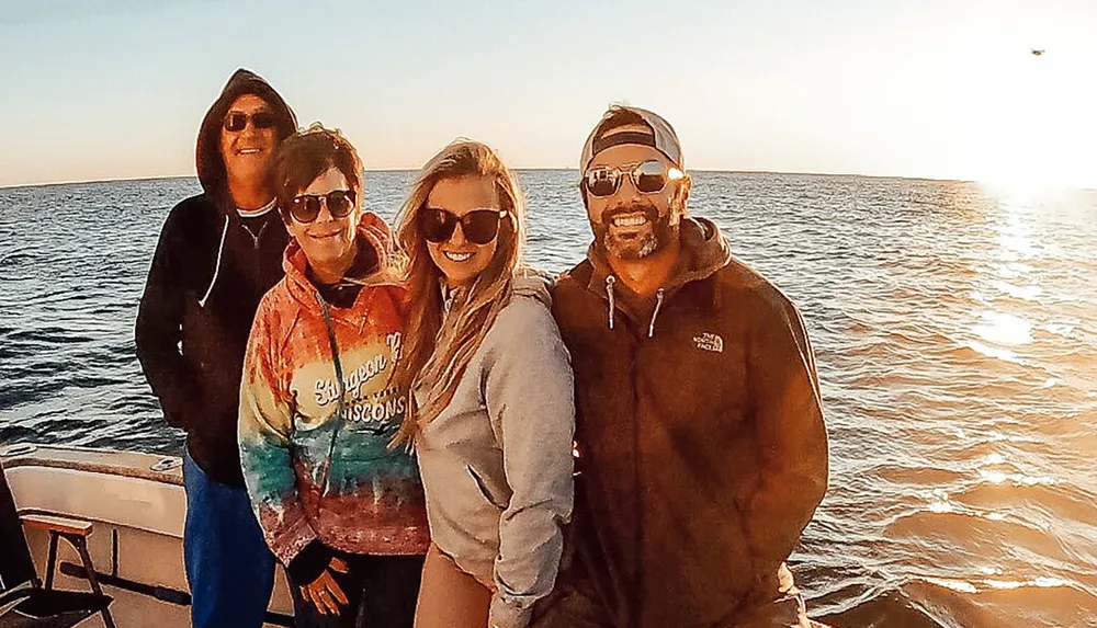 Four people are smiling for a photo on a boat with the sun setting over the water in the background