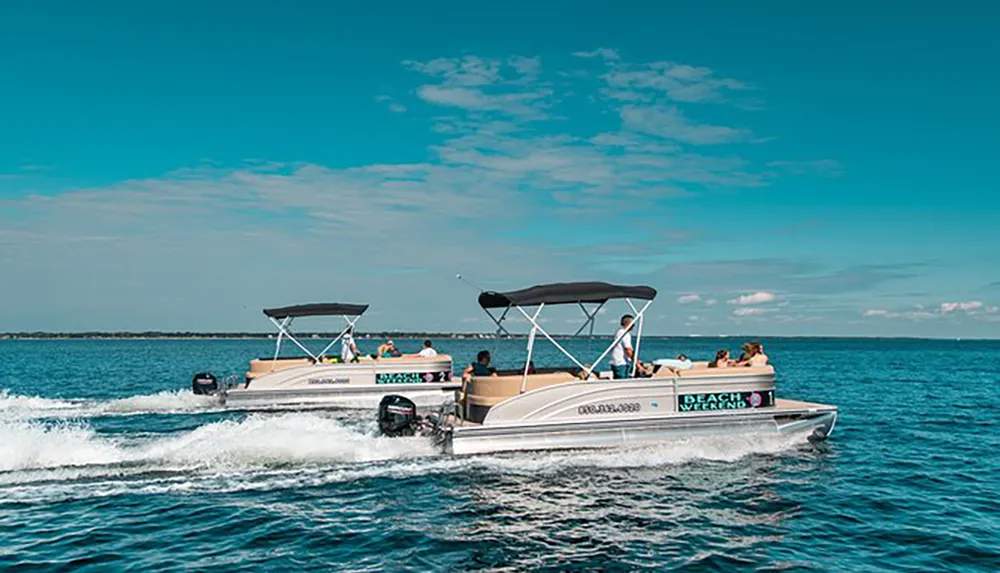 Two pontoon boats with passengers are cruising side by side on a clear sunny day on the water