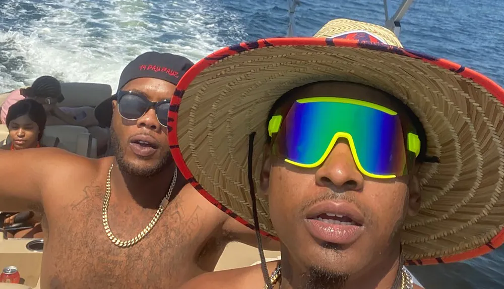 Two men wearing sunglasses are taking a selfie on a boat with the ocean in the background
