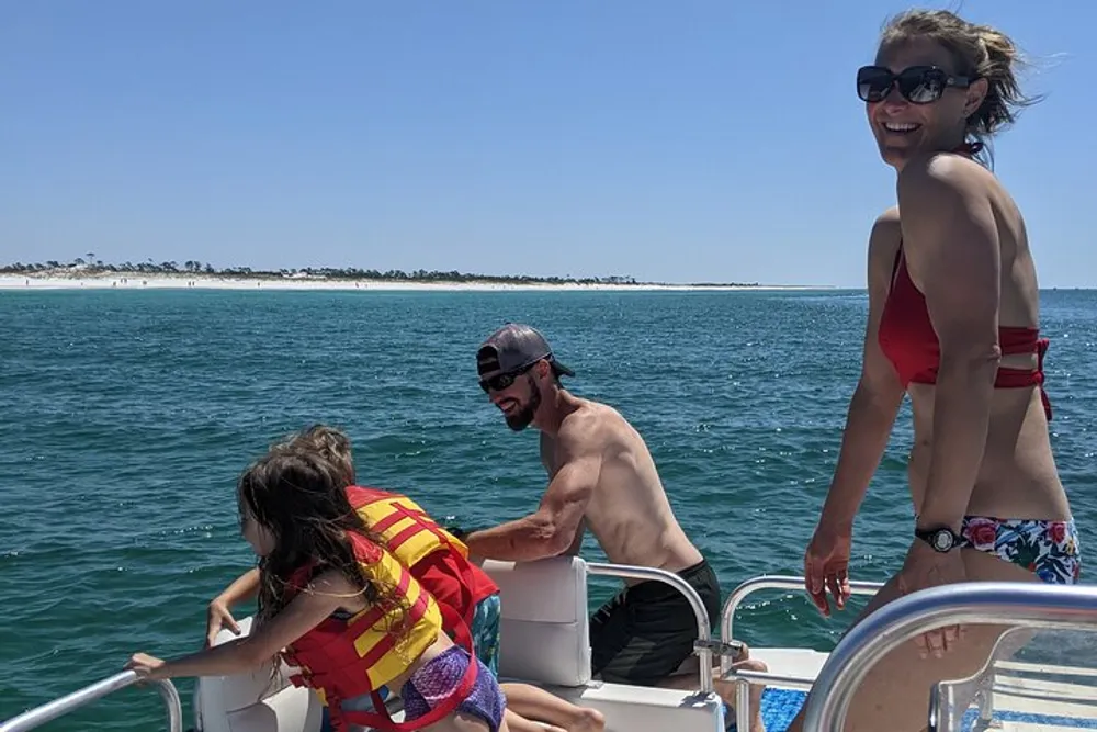 Three people are enjoying a sunny day on a boat with a woman in red ready to jump into the water while a man assists her and another woman smiles at the camera