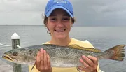 A smiling person is holding a large fish in front of a body of water.