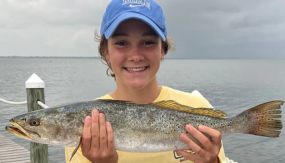 A smiling person is holding a large fish in front of a body of water