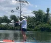 A person is paddleboarding on calm water with lush greenery in the background