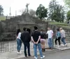 A group of people are standing near a fenced-off statue in what appears to be a cemetery