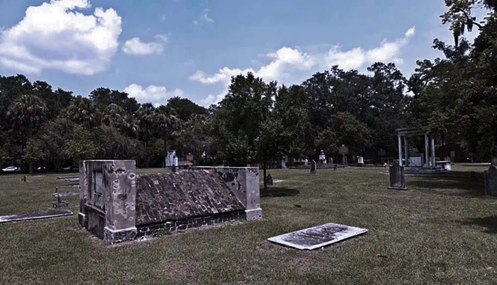 The image shows an old cemetery with various tombstones and monuments under a cloudy sky