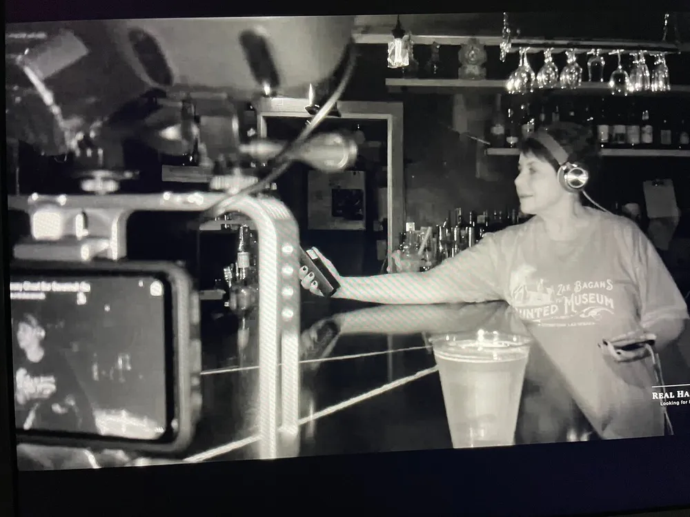 A person wearing headphones stands at a bar as seen on an infrared camera screen indicating a possible paranormal investigation setup
