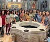 A group of women are posing for a photo around a baptismal font inside a beautifully decorated church