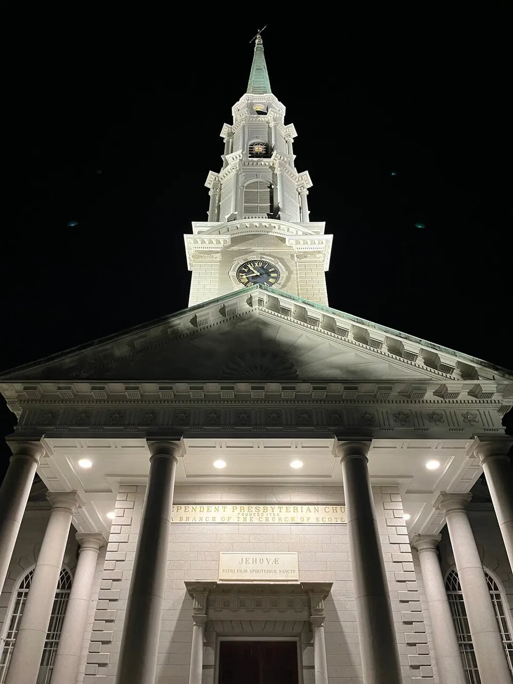 The image shows the illuminated facade of the Independent Presbyterian Church at night highlighting its classical architecture and prominent steeple with a clock