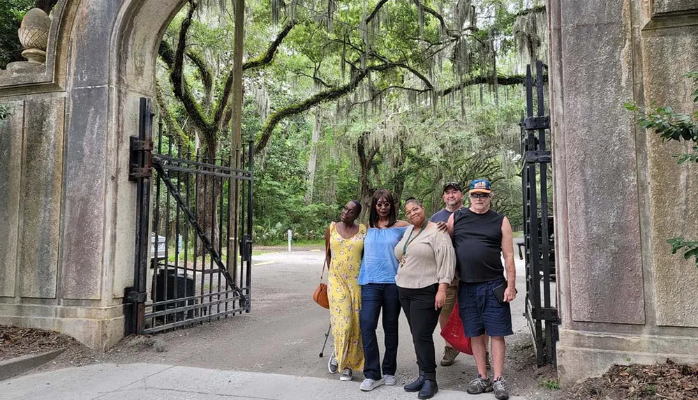 A group of people are posing for a photo at an open gate surrounded by lush greenery and draped Spanish moss