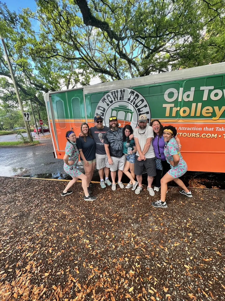 A group of cheerful people is posing for a photo in front of an Old Town Trolley Tours vehicle.