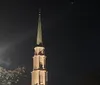 The image shows a church steeple illuminated against the night sky with a clear view of the architectural details and a light source visible to the left