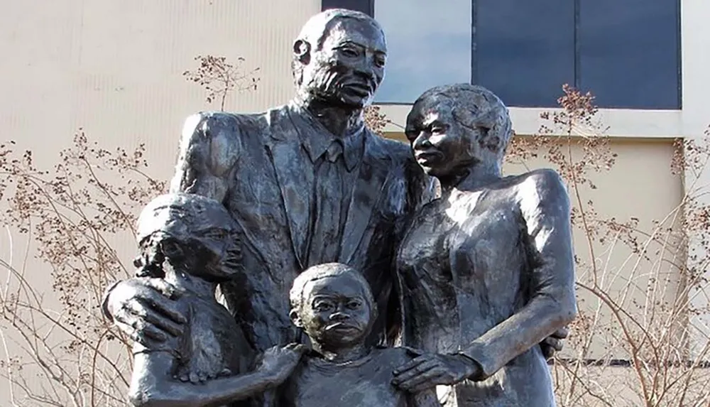 This image shows a bronze statue of a family with two adults and two children displayed outdoors