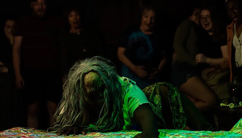 A person in horror-themed makeup or costume is crawling on a table in front of a visibly shocked and entertained audience