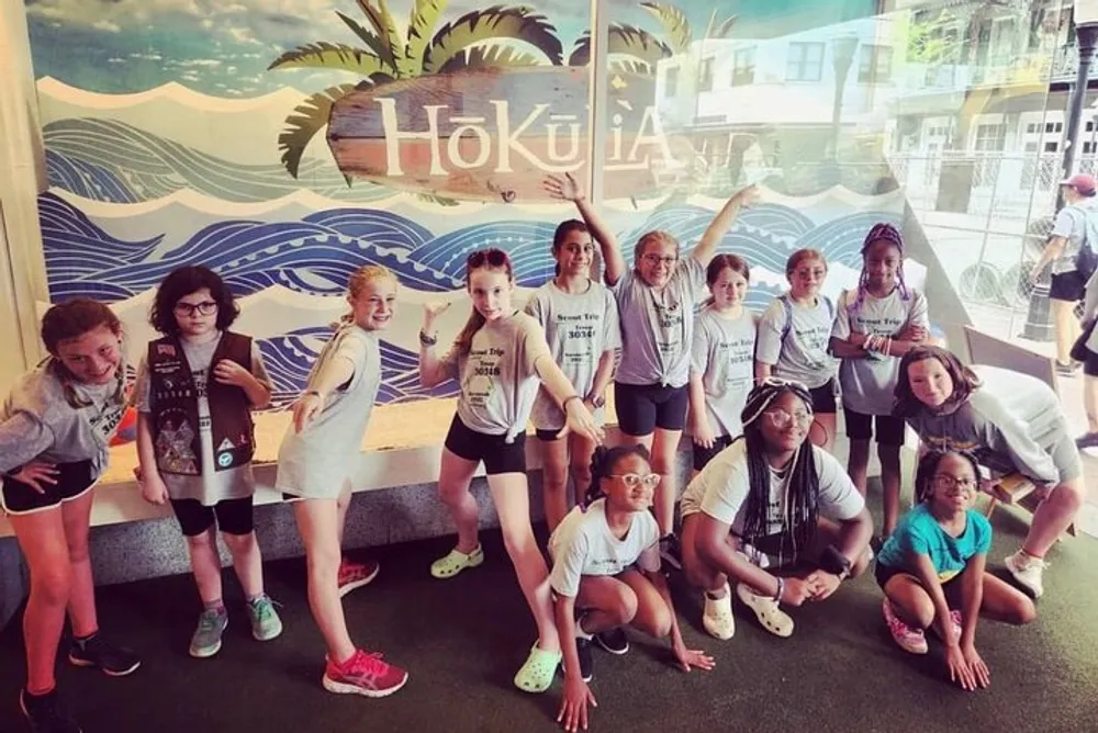 A group of smiling children possibly a sports team or youth group is posing for a photo in front of a mural with ocean waves and the text Hklea