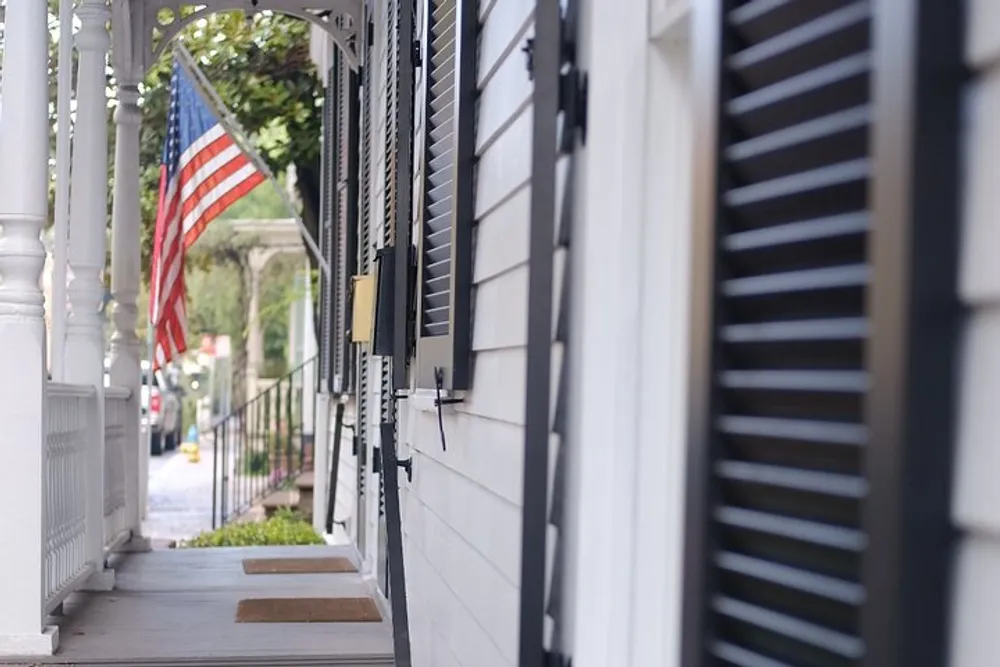 A shallow depth-of-field photo capturing the side of a building with black shutters and an American flag hanging in the background