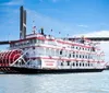 A paddlewheel riverboat named Georgia Queen is cruising on a river with a modern bridge in the background under a blue sky