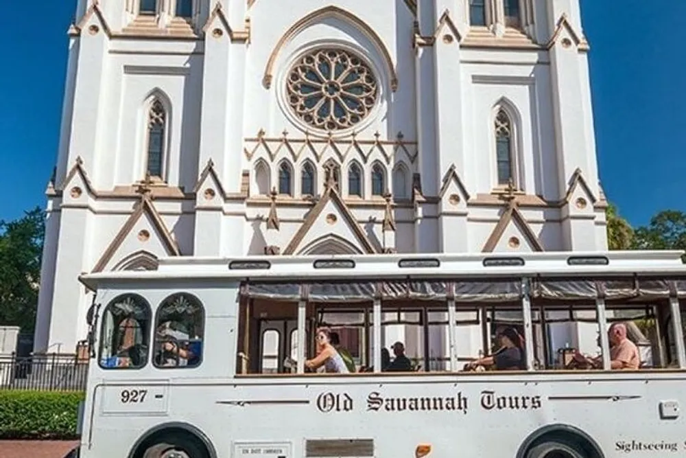 A tour bus labeled Old Savannah Tours is parked in front of a large ornate white church with Gothic architectural features under a clear blue sky