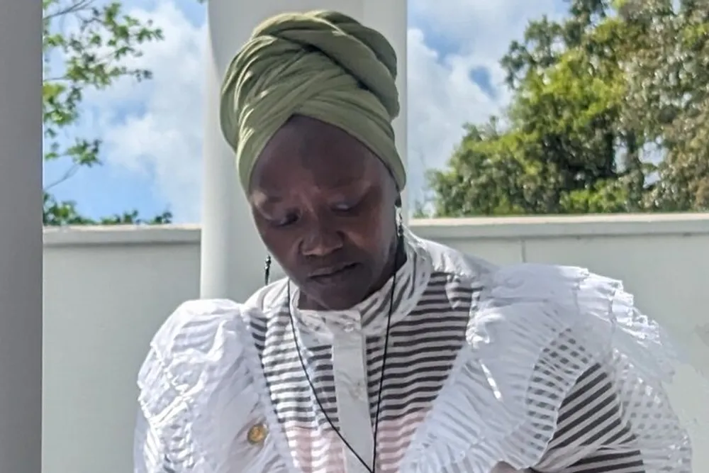 A woman wearing a green headwrap and a white ruffled blouse seems focused on something out of frame