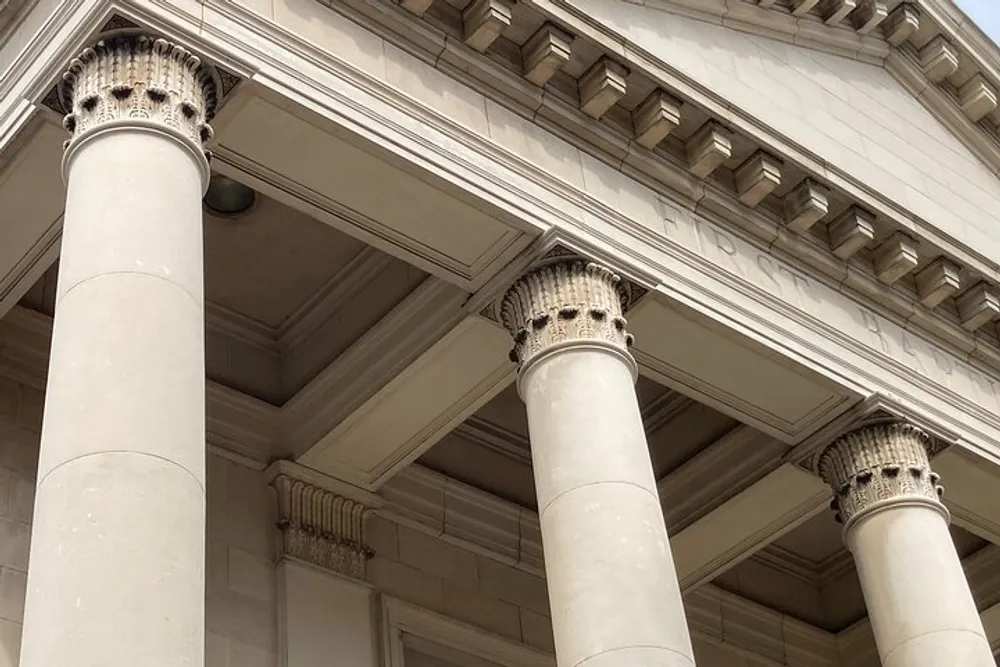 The image shows a close-up of a classic architectural structure with a focus on Corinthian columns supporting a detailed entablature