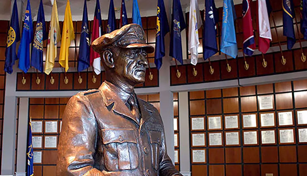 A bronze statue of a military figure is displayed in a room adorned with various flags and plaques on the wall