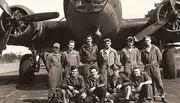 A group of nine uniformed military personnel poses in front of a twin-engine bomber aircraft, likely from the World War II era.