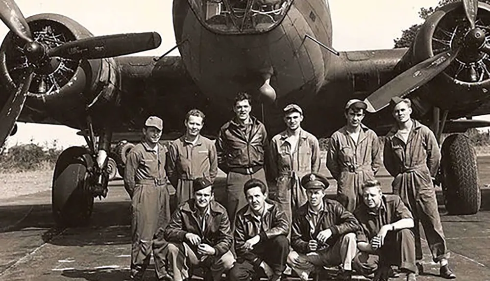 A group of nine uniformed military personnel poses in front of a twin-engine bomber aircraft likely from the World War II era