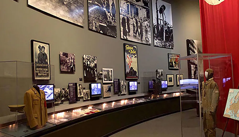 This image shows an exhibition space with historical photographs display cases containing artifacts and a mannequin dressed in a military uniform likely part of a museum dedicated to history or military events