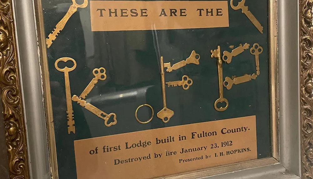 The image shows a framed collection of antique keys with an inscription stating they are from the first Lodge built in Fulton County destroyed by fire in 1912