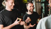 Two men are smiling and holding slices of lime and a shot glass, appearing to be enjoying a social moment at a bar.