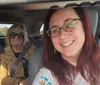Three smiling women are seated in a car with the driver taking a selfie of the group