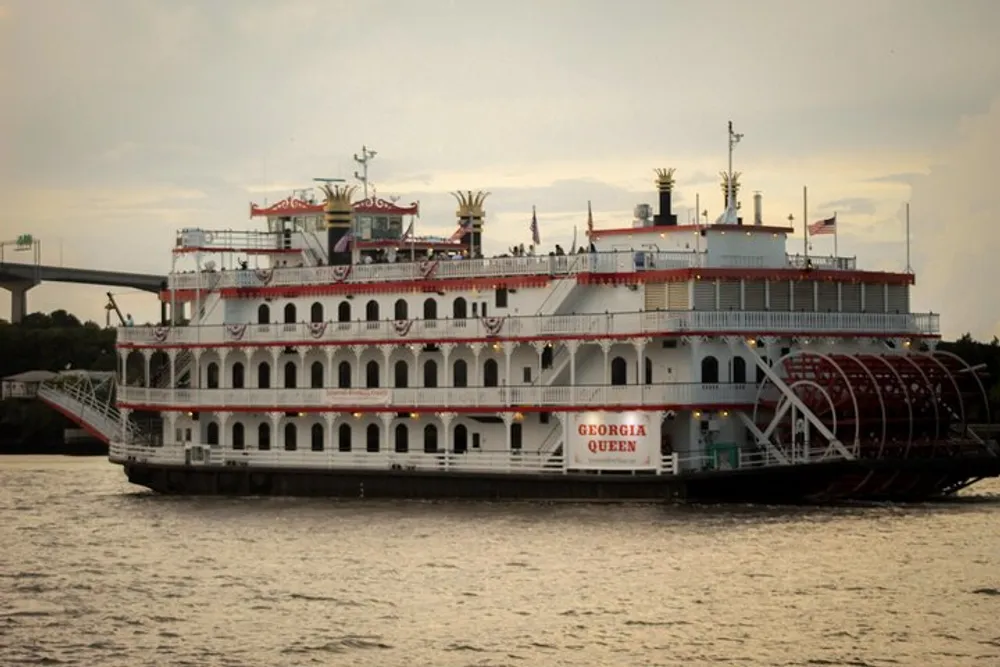 The image shows the paddlewheel riverboat Georgia Queen floating on the water featuring multiple decks and a large red paddlewheel on the side